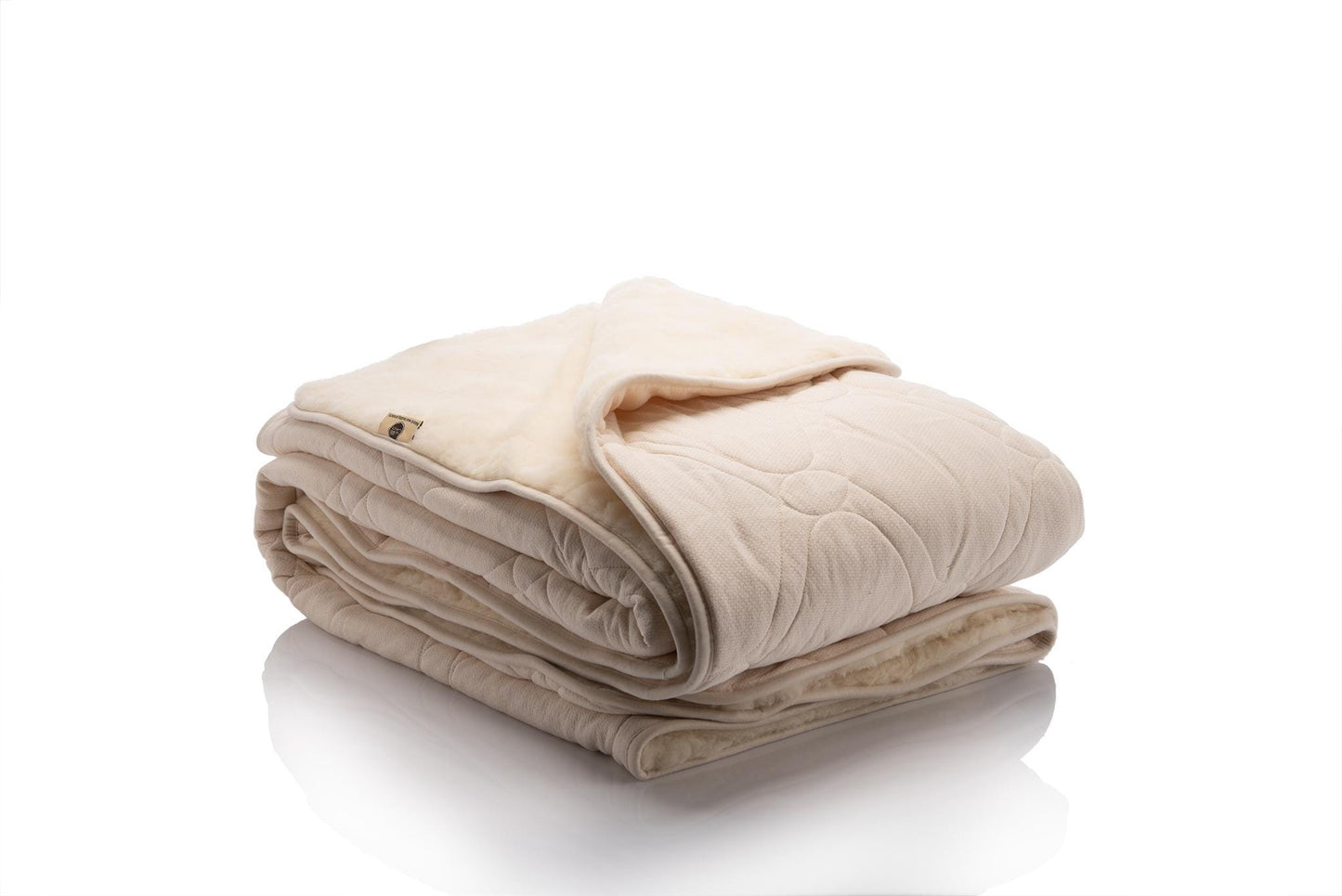 Reversible blanket with one side in soft cream organic cotton quilted with wool padding and the other side in natural beige merino wool, shown folded to highlight both textures.