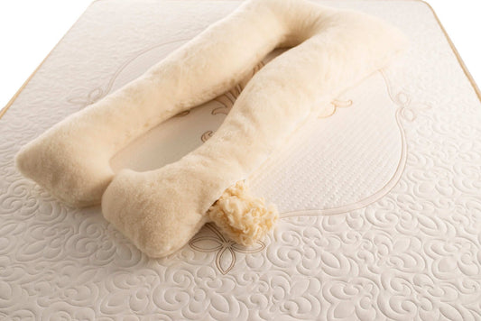 A beige, u-shaped full body merino wool pillow on a bed, designed for pregnancy support.